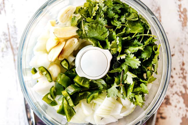 showing how to make mojo marinade by adding onion, garlic, cilantro and jalapeno to food processor