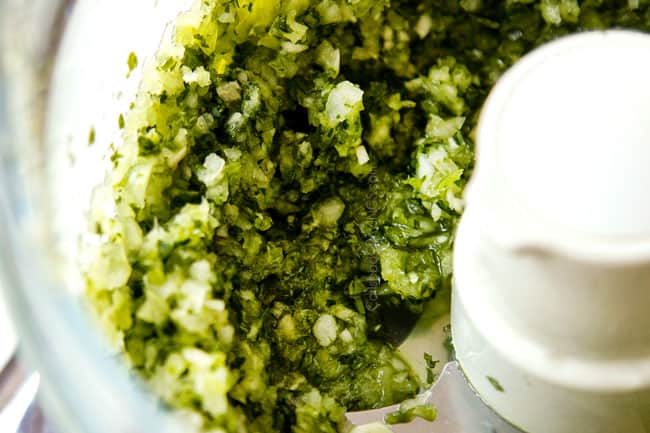 showing how to make mojo marinade by finely chopping onion, garlic, cilantro and jalapeno in food processor