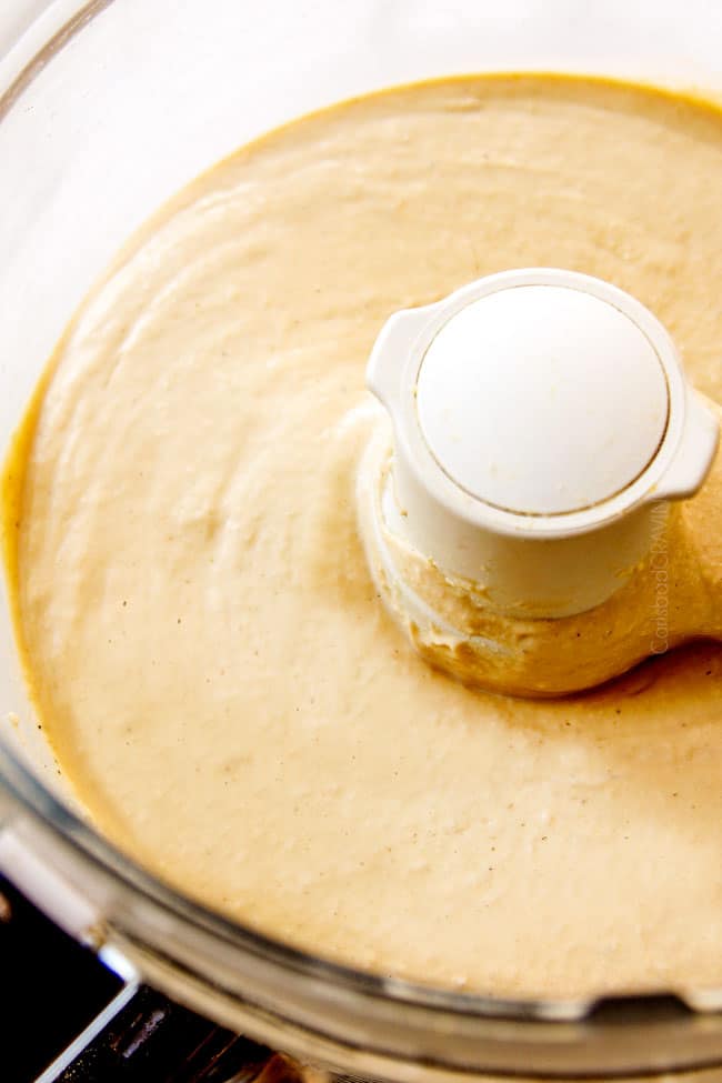 up close side view showing how to make hummus by blending hummus until smooth in the food processor