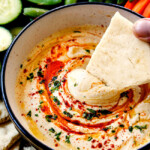 showing how creamy homemade hummus is by dipping pita bread into it