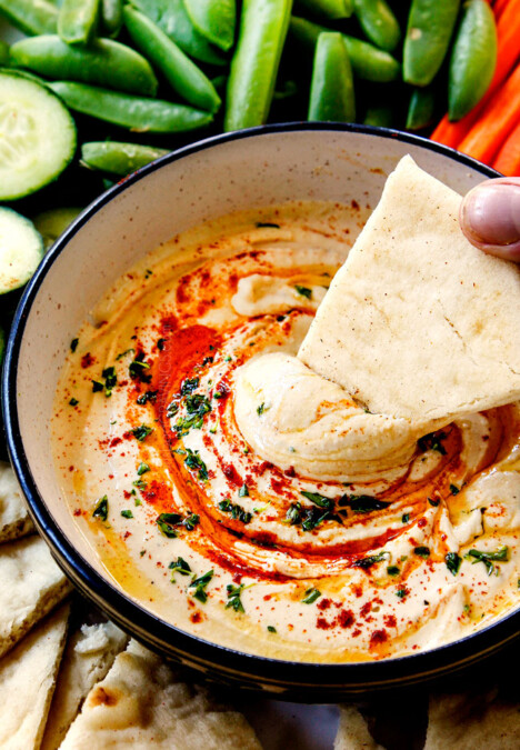 showing how creamy homemade hummus is by dipping pita bread into it