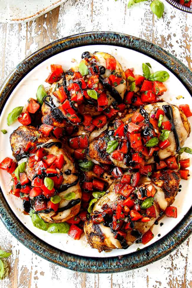 showing how to make Bruschetta Chicken recipe by adding chicken to a white plate and topping with bruschetta chicken and balsamic glaze 