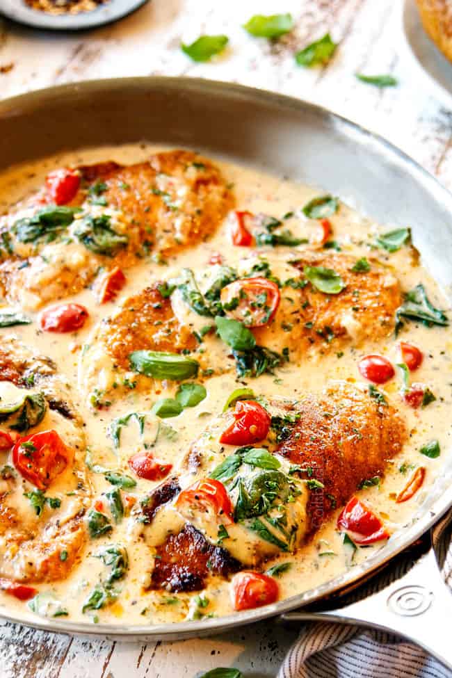 showing how to make  Chicken Florentine by spooning cream spinach sauce over chicken cutlets in a stainless steel pan