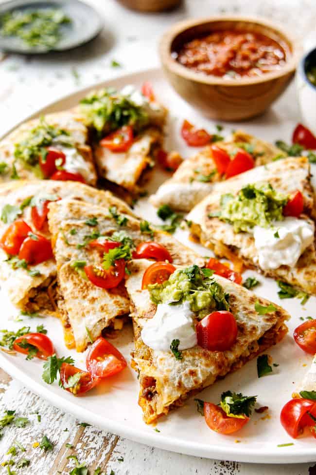 up close of breakfast quesadillas cut into wedges on a white platter with dollops of sour cream and guacamole