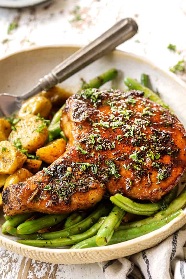 up close of a baked brown sugar pork chop served with green beans and potatoes in a tan dishh