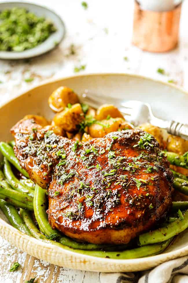 up close of brown sugar pork chops baked in the oven in a tan dish with green beans and potatoes