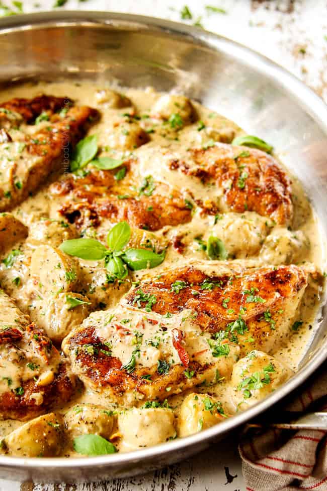 up close creamy Tuscan chicken breast in a stainless steel skillet garnished by parsley and basil 