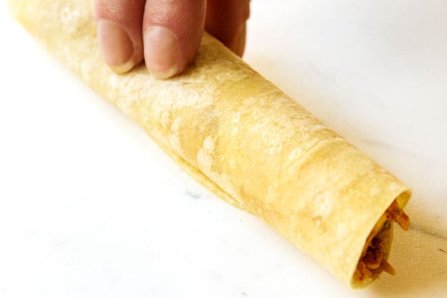 showing how to make flautas by rolling chicken filling in a flour tortilla