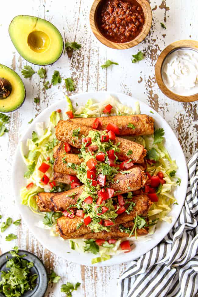 top view of  flautas on a white plate with shredded lettuce, guacamole and chopped tomatoes
