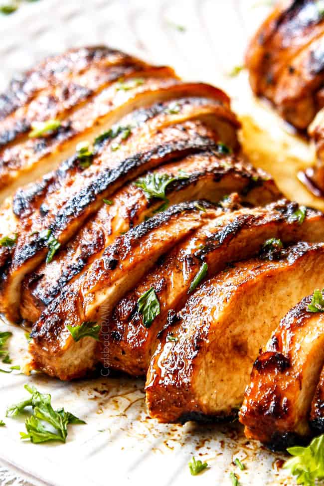 up close side view of sliced easy marinated grilled chicken on a white plate showing how juicy it is