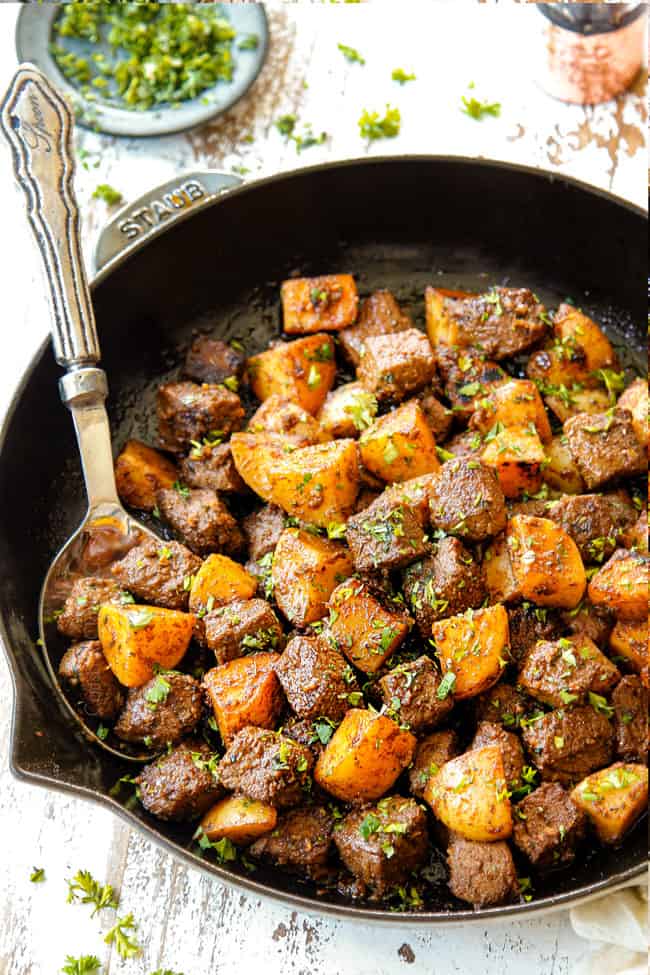 showing how to make garlic butter steak and potatoes skillet by combining steak bites and potatoes in a cast iron skillet