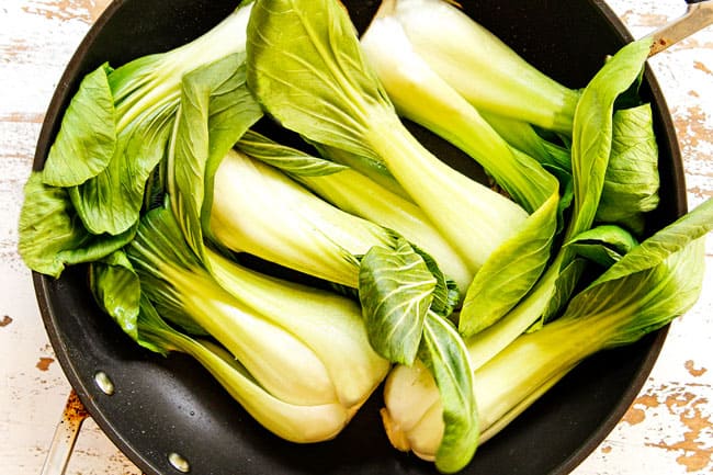 showing how to cook bok choy by adding baby bok choy cut side down in a black nonstick skillet