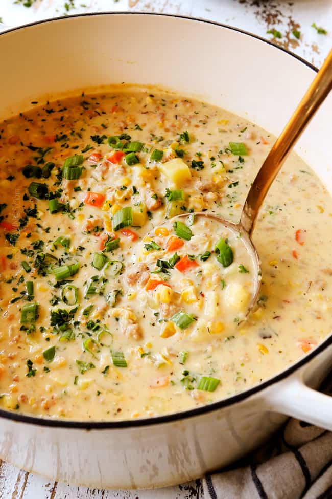 corn chowder recipe in a white soup pot being scooped up with a ladle
