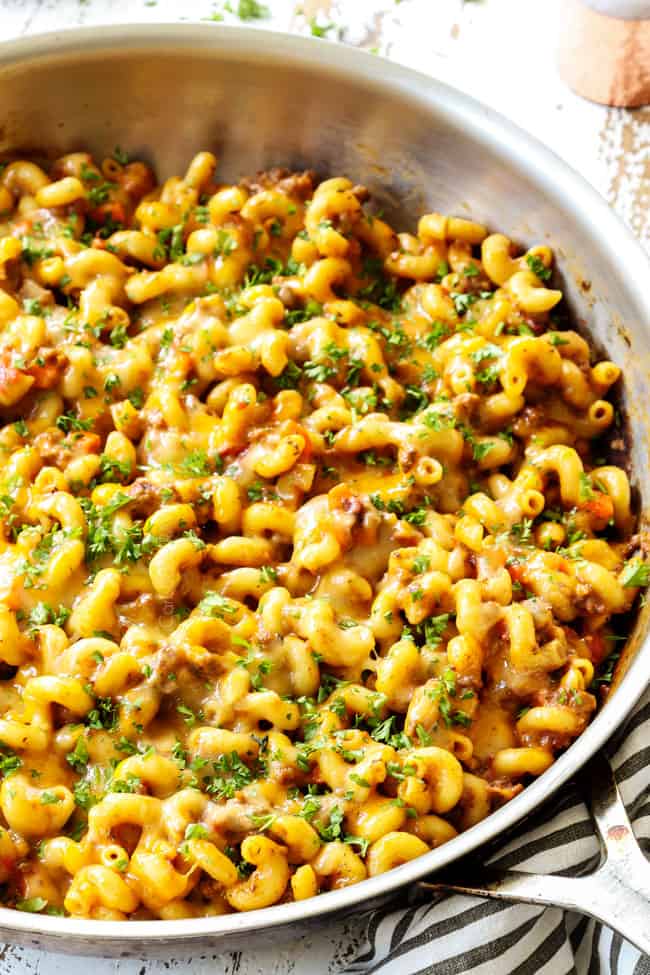 a skillet of hamburger helper recipe covered in cheese garnished with parsley