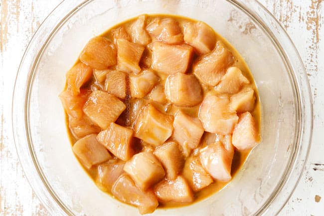 showing how to make honey garlic chicken recipe by marinating cubed chicken breasts in a glass bowl