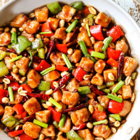 top view of kung pao chicken in a white skillet garnished with green onions