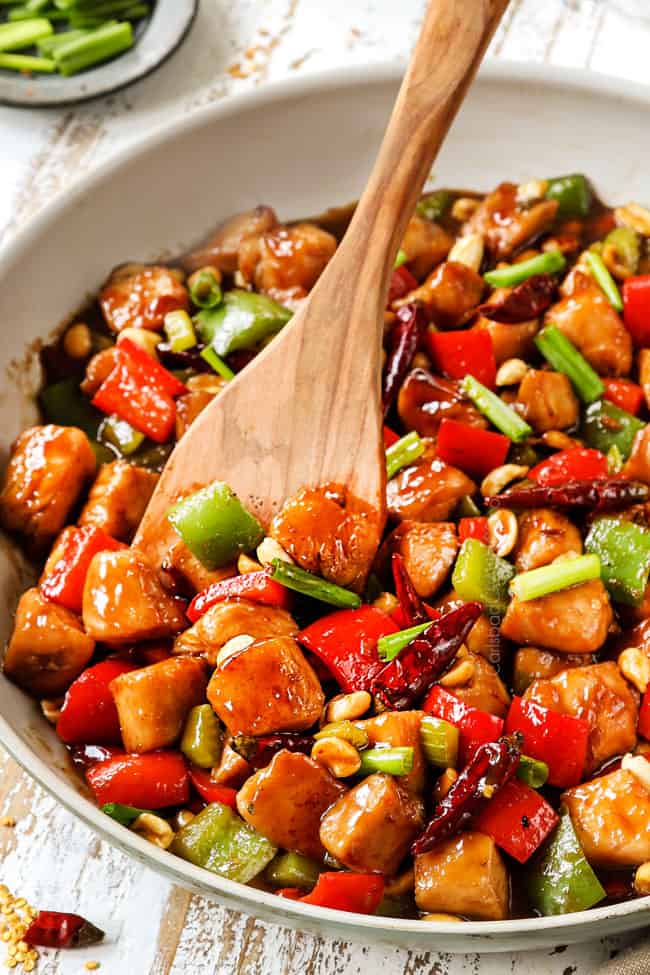 a wooden spatula serving best kung pao chicken  form a white skillet