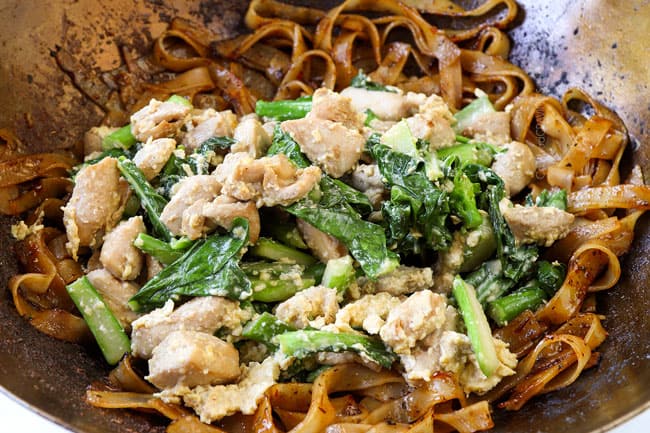 showing how to make pad see ew recipe by adding stir fried chicken, Chinese broccoli and eggs with the stir fried noodles