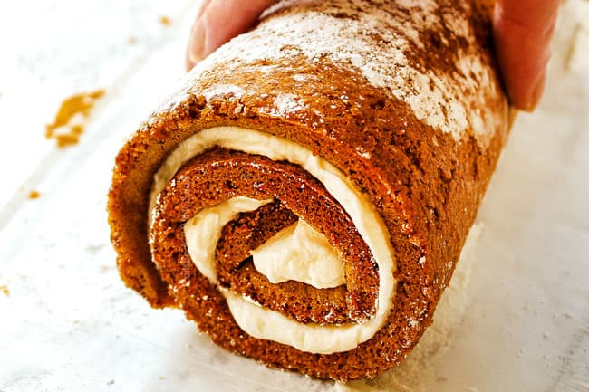 showing how to make a pumpkin roll by rolling up the cake tightly with cream cheese filling