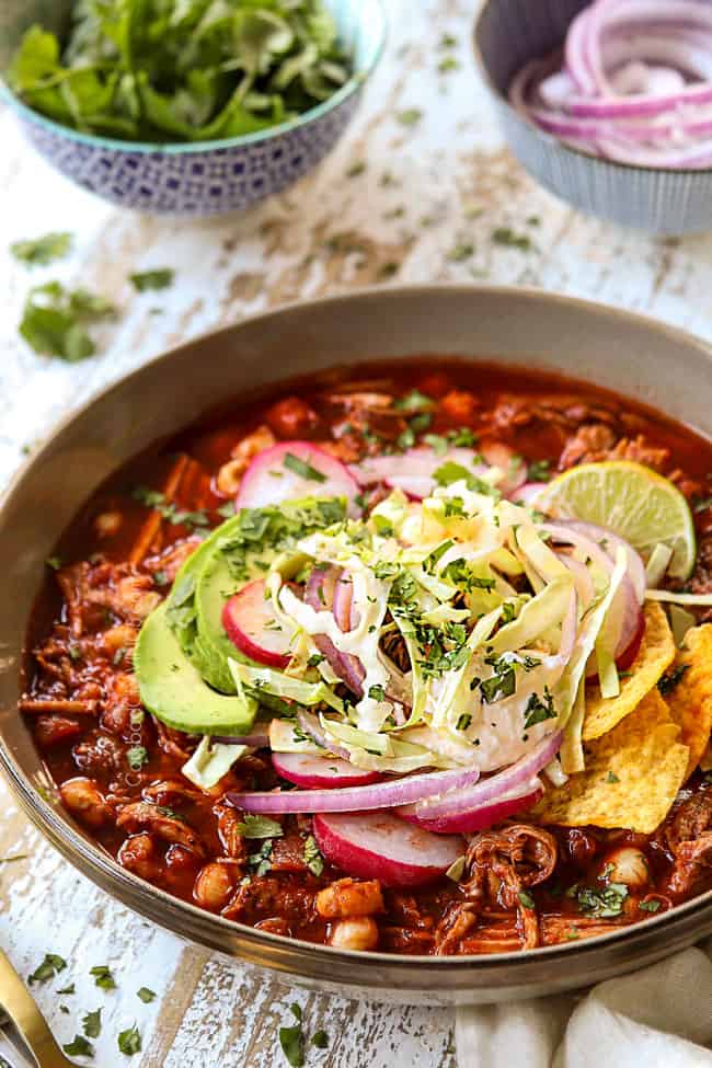up close of a bowl of pozole rojo garnshid with cilantro, limes, red onions, radishes