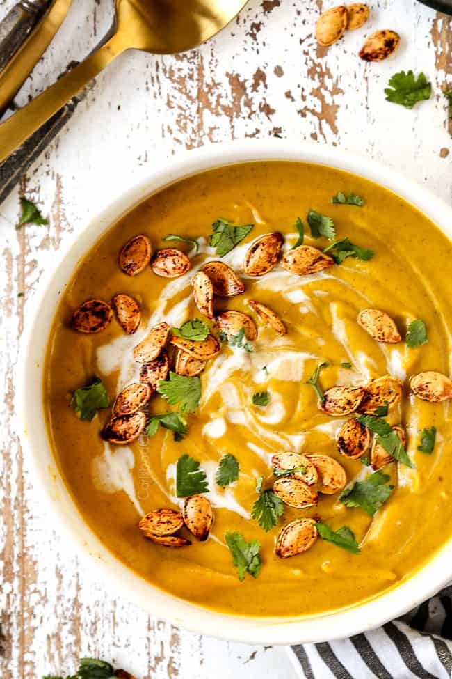 top view of pumpkin soup ripe in a white bowl garnished with coconut milk, cilantro and pumpkin seeds