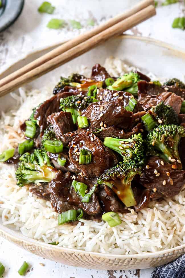 showing how to serve crockpot beef and broccoli recipe by adding to a bowl of white rice and garnishing with green onions and sesame seeds 
