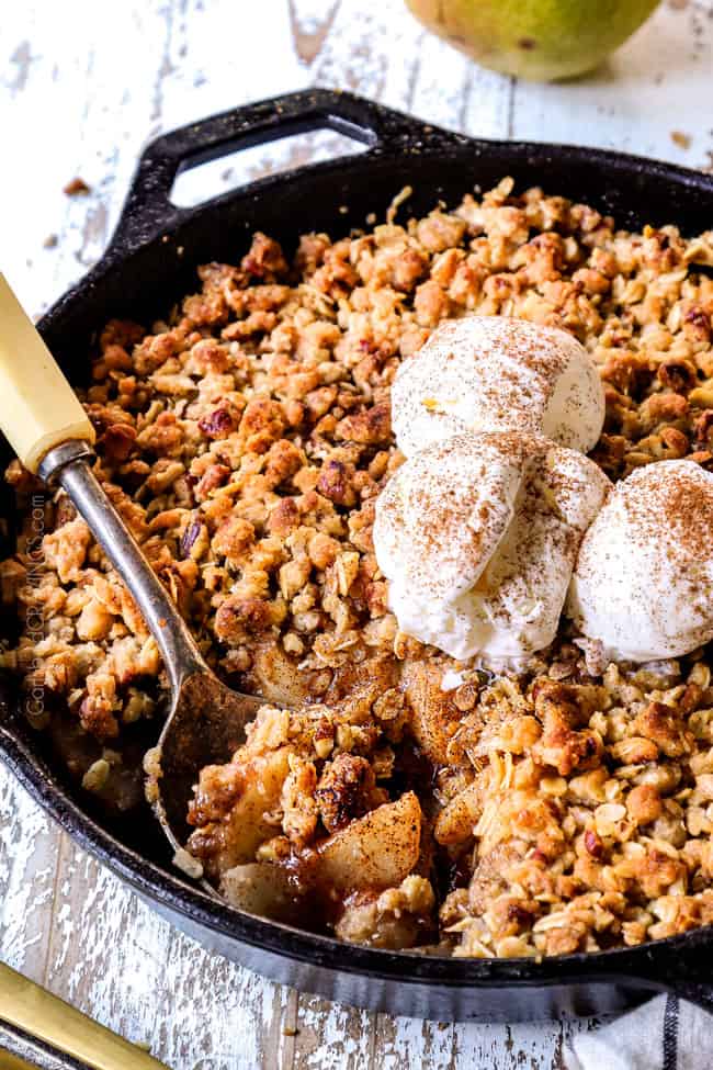 scooping a serving of pear crisp in a cast iron skillet with pecan crumble topping