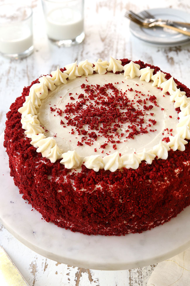  red velvet cheesecake recipe on a white pedestal decorated with red velvet crumbs