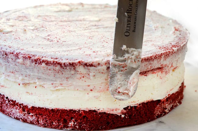 showing how to make red velvet cheesecake by frosting with a small amount of frosting to create a crumb layer