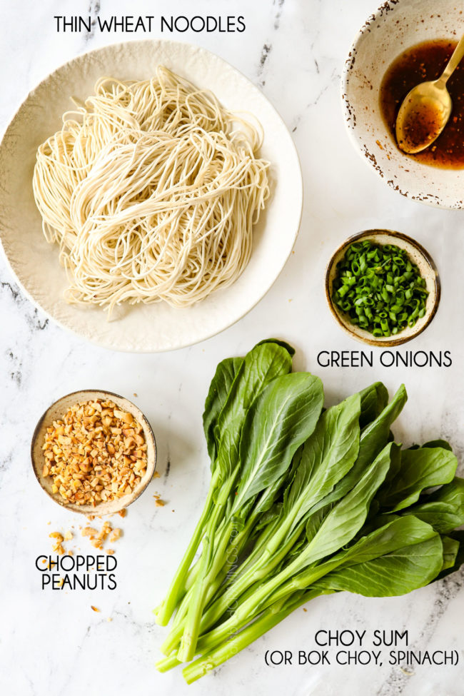 showing how to make Dan Dan Noodles recipe by lining up noodles, choy sum, chopped peanuts and green onions