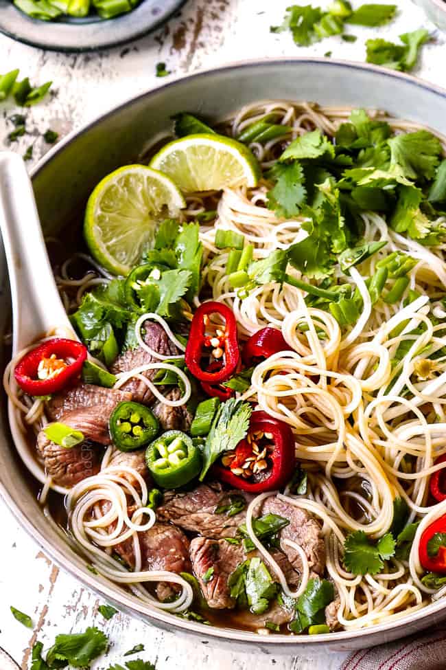 beef pho soup in a bowl garnished with chili peppers, bean sprouts, lime wedges and cilantro
