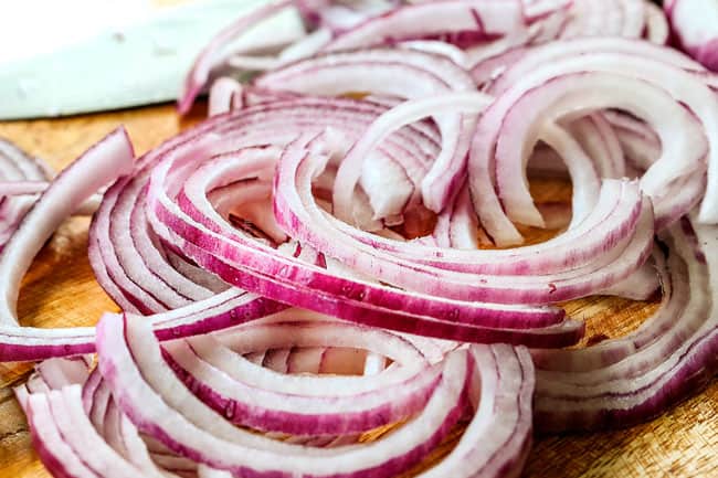 showing how to pickle red onions by slicing red onions 1/8-inch thick on a wood cutting board