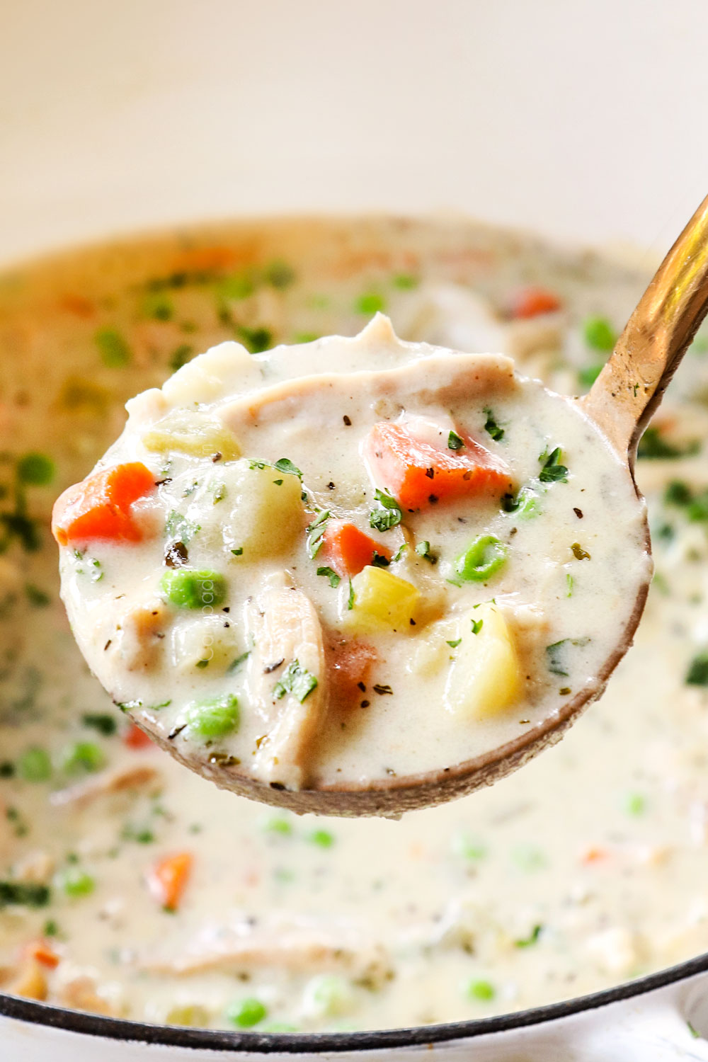 up close of a ladle of chicken pot pie soup with chicken, carrots and celery