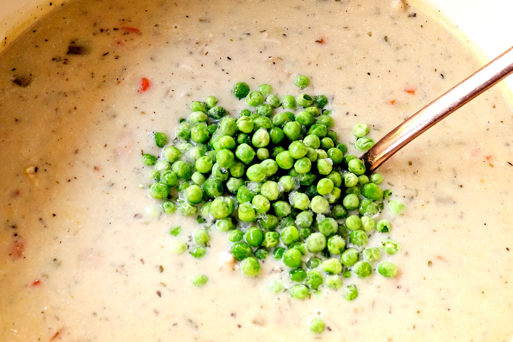 showing how to make chicken pot pie soup by adding peas to soup