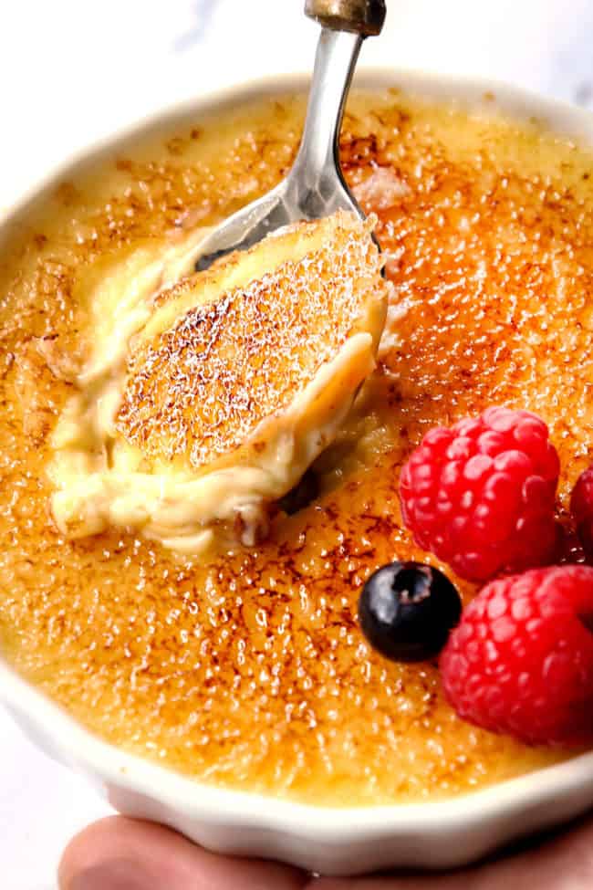 a hand holding best crème brûlée recipe with a spoon taking a bite showing the carnalized sugar topping