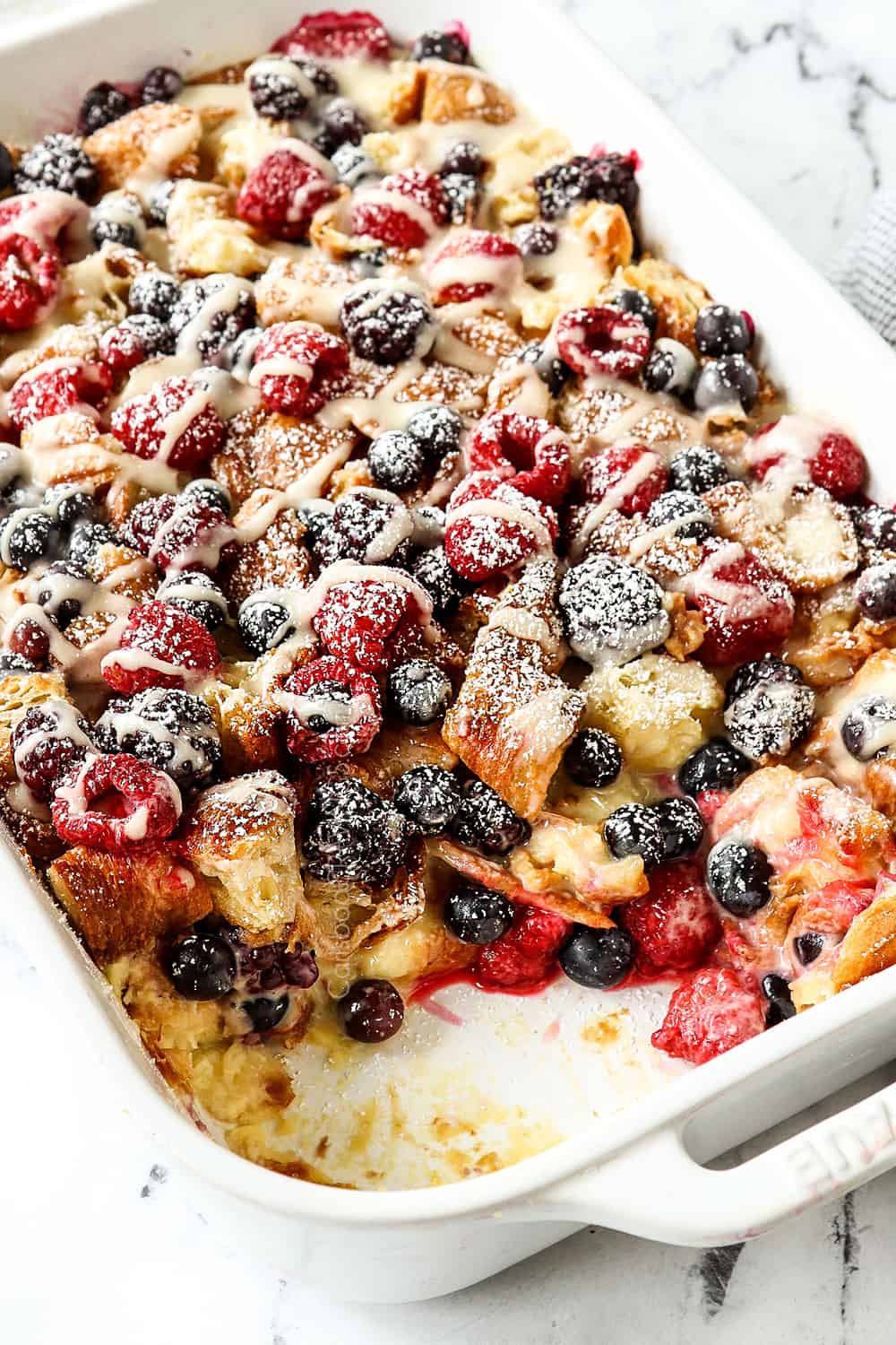breakfast bake with pieces missing so you can see the inside of the breakfast casserole with croissants and berries
