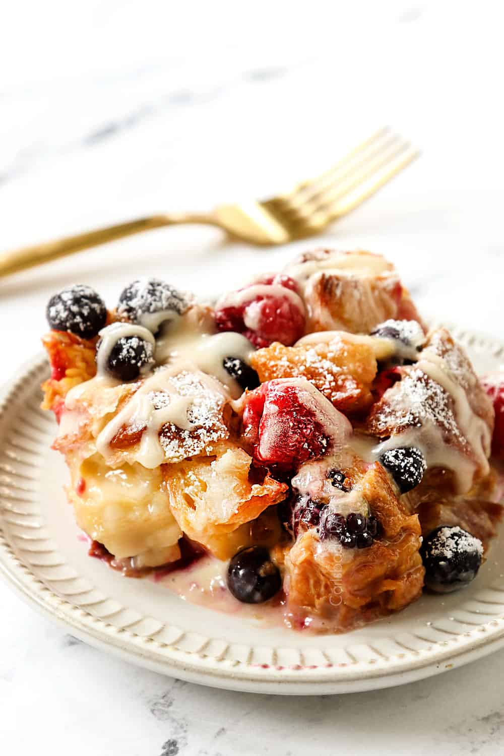 a slice of sweet croissant breakfast casserole on a plate with berries