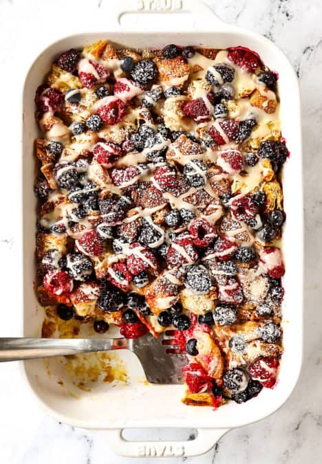 top view of sweet breakfast casserole with croissants, berries and lemon drizzle in a white casserole dish