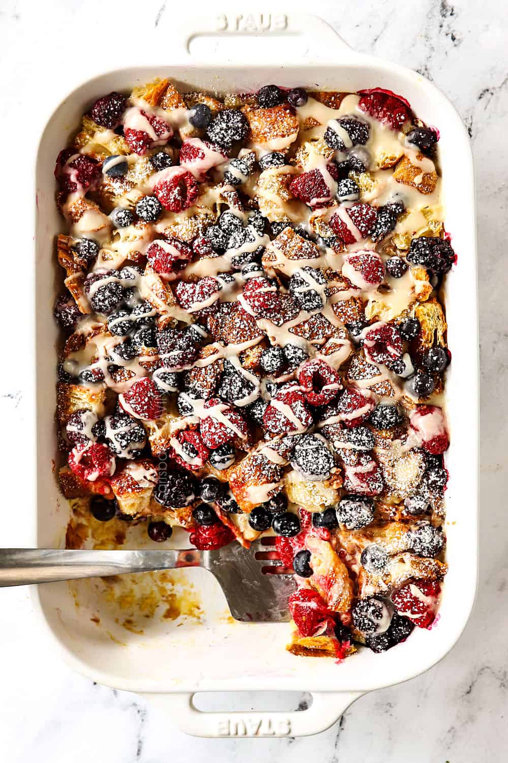 top view of sweet breakfast casserole with croissants, berries and lemon drizzle in a white casserole dish