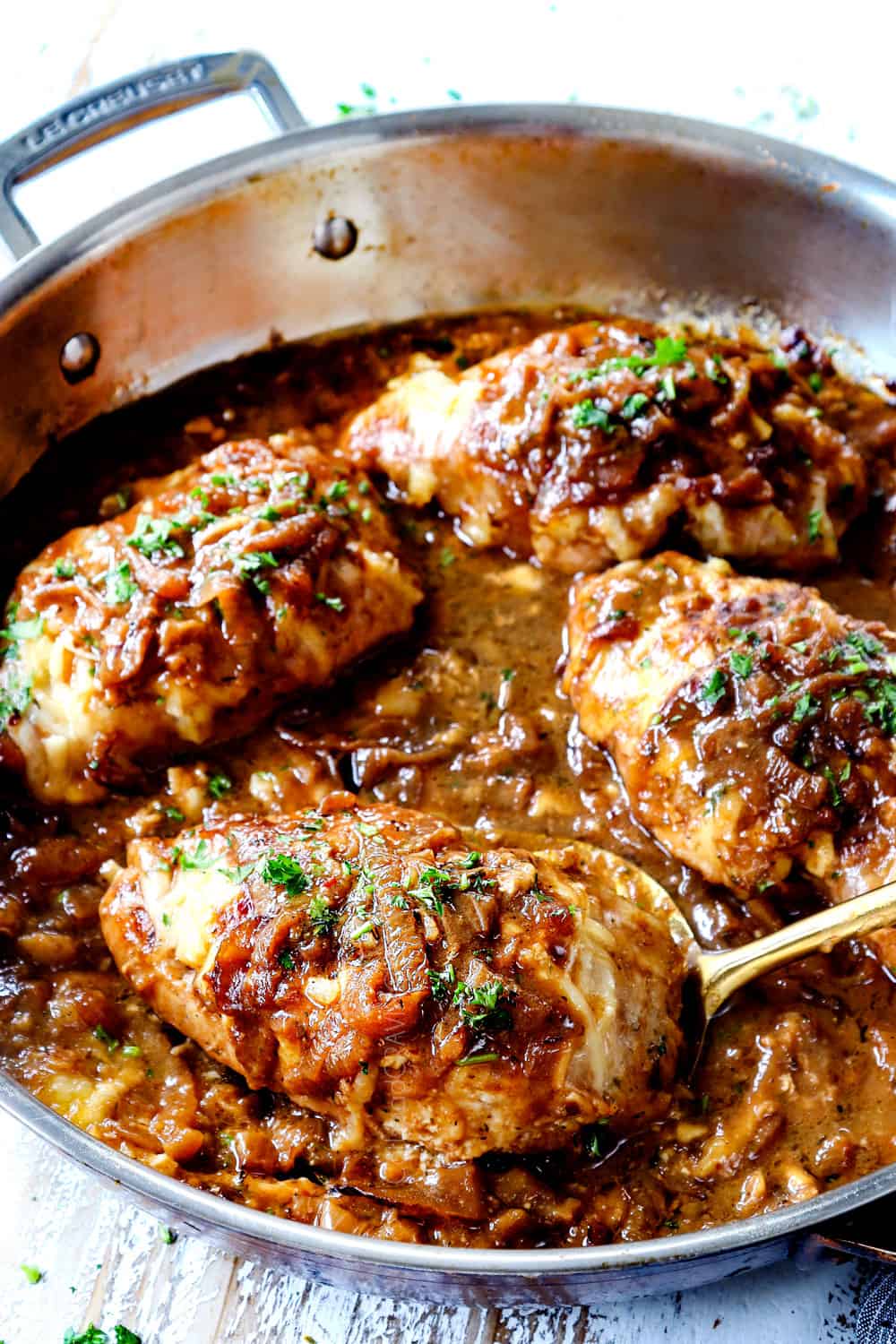 French onion chicken in a skillet with a ladle picking up a piece