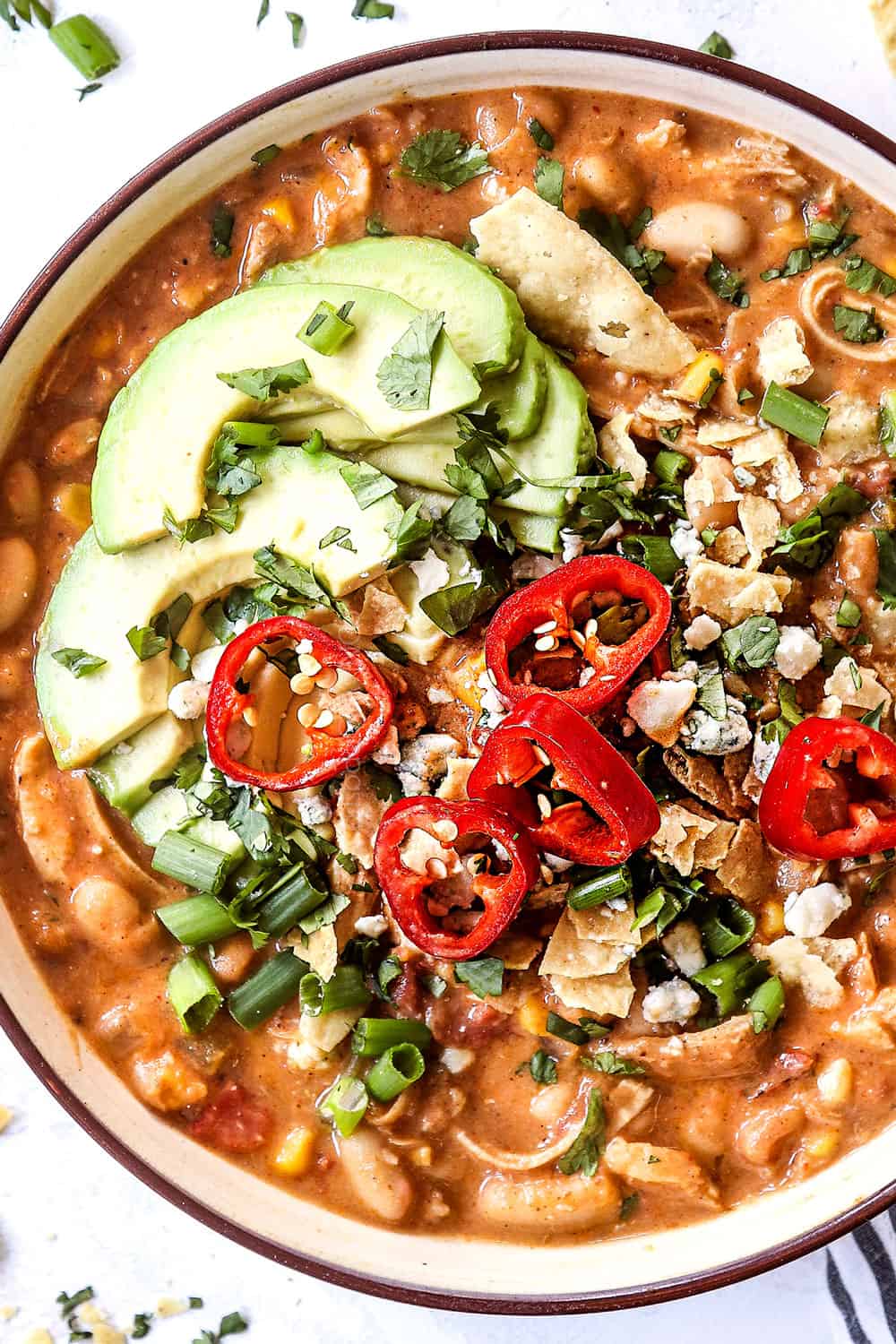 showing how to top a bowl of buffalo chicken chili by adding chips, blue cheese and avocados 