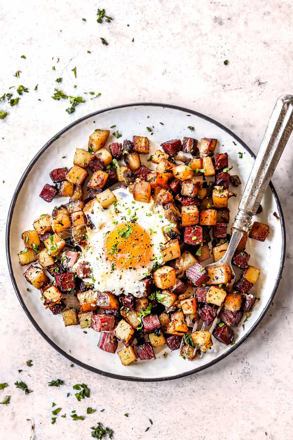 showing how to serve homemade corned beef hash recipe by adding hash to a plate and topping with a sunny side up egg