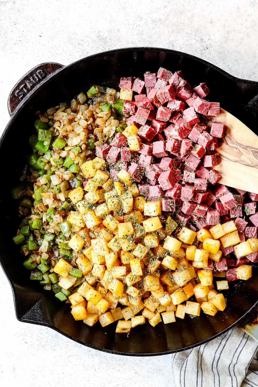 showing how to make corned beef hash by adding corned beef, diced potatoes and onions to a skillet