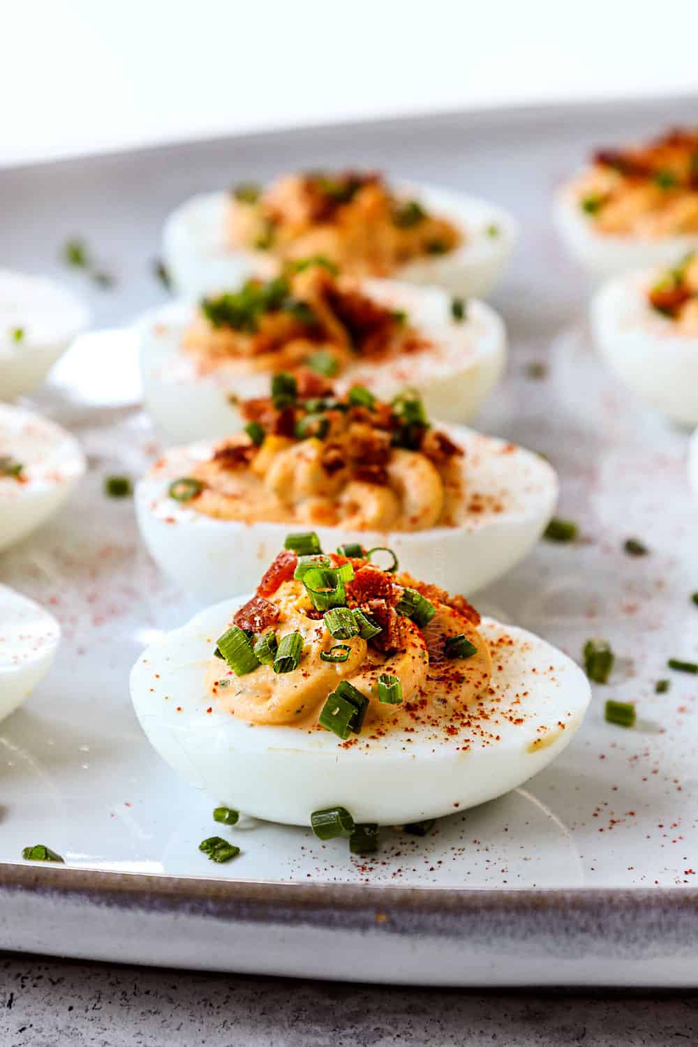 side view of deviled eggs recipe on a platter with bacon and chives  