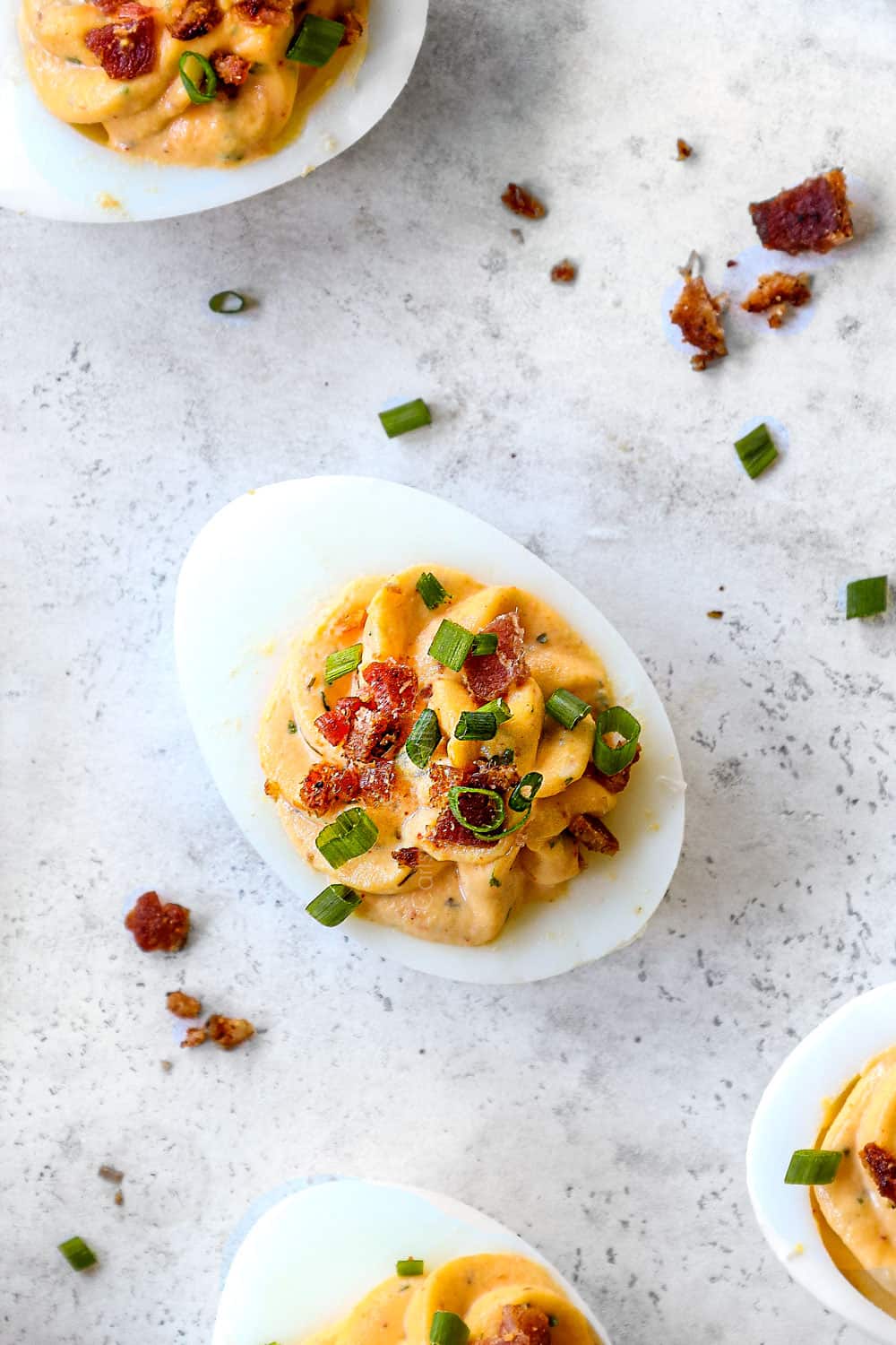showing how to make deviled eggs by adding bacon and chives to top of the eggs