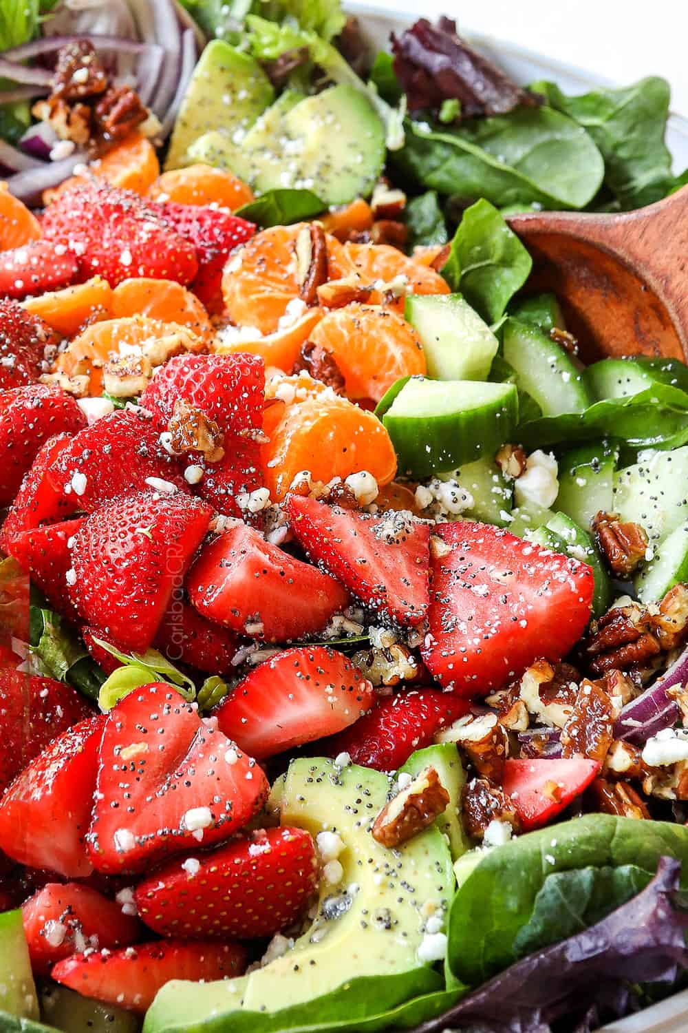 showing how to make strawberry spinach salad recipe by tossing ingredients together in a bowl