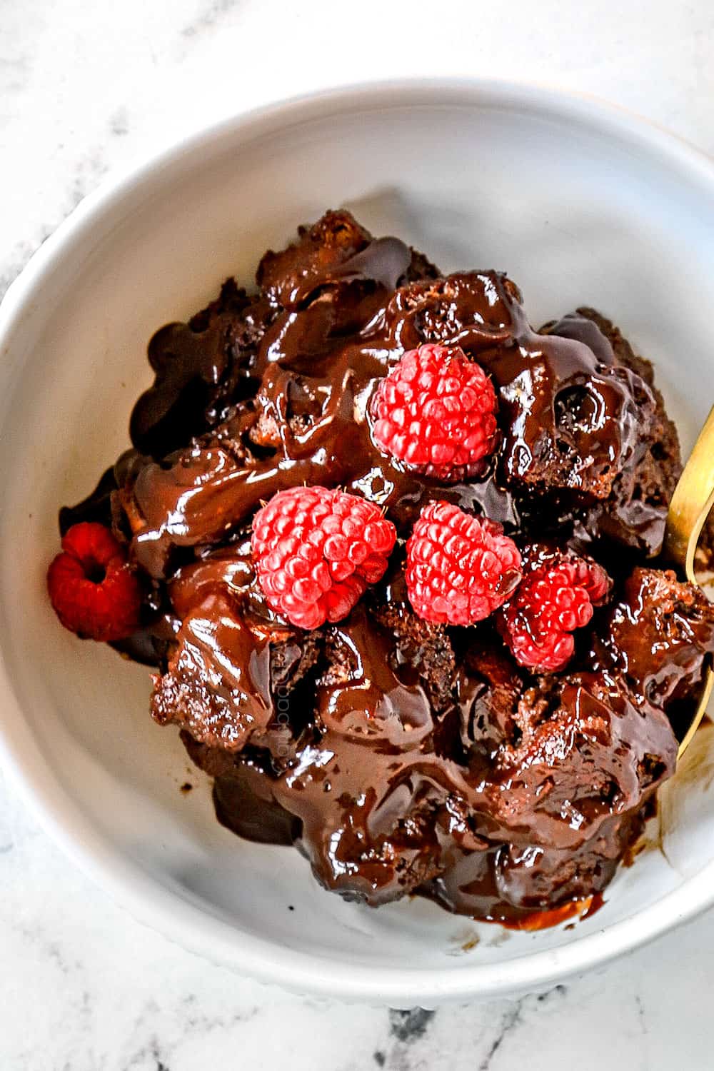 top view of chocolate bread pudding recipe in a white bowl garnished with raspberries