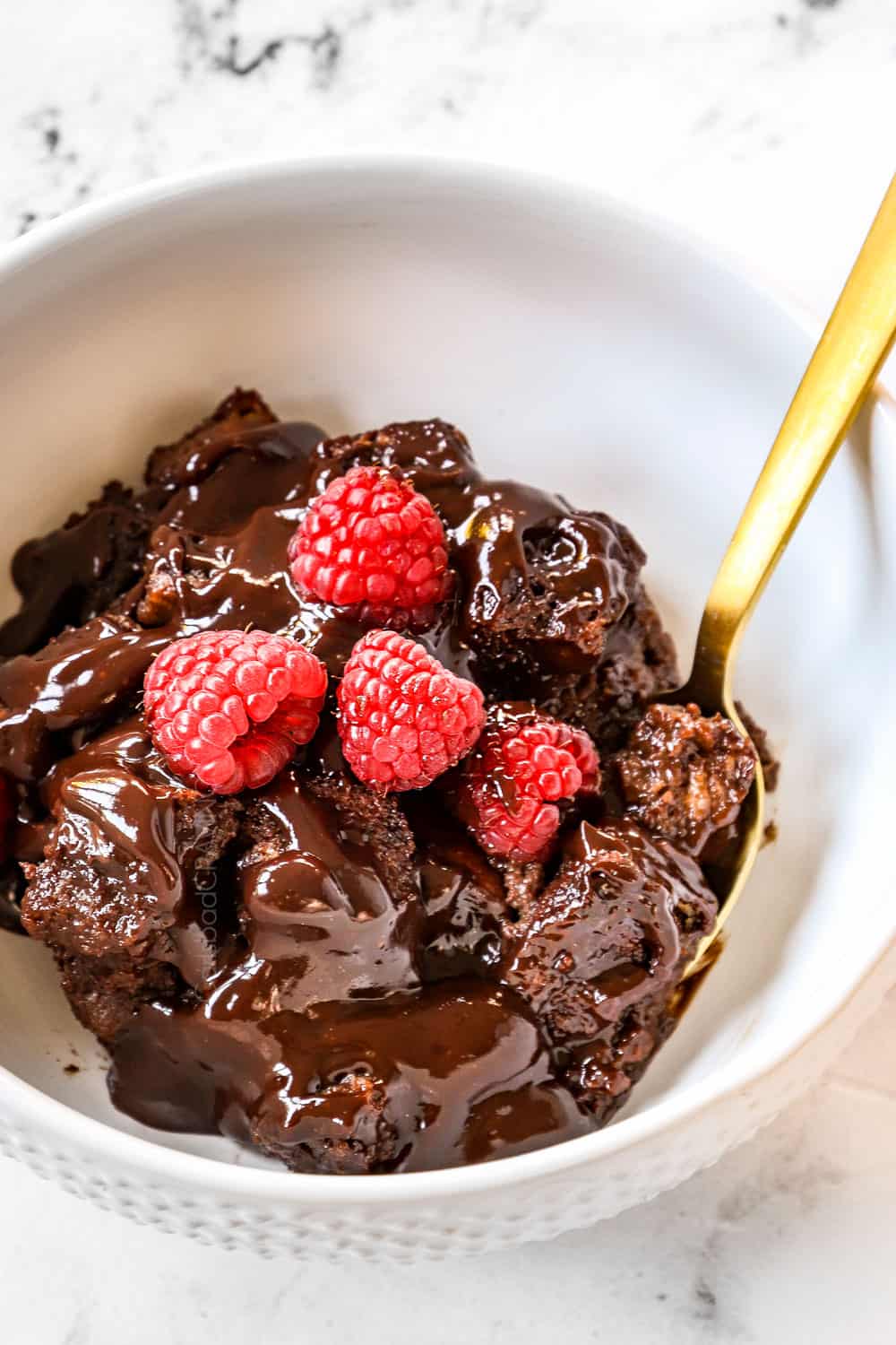 showing how to serve chocolate bread pudding by serving in a white bowl with chocolate sauce and raspberries