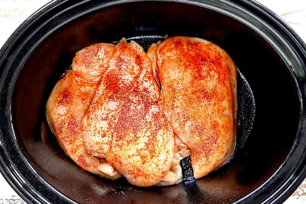 showing how to make crockpot chicken and gravy by adding seasoned chicken breasts to the bottom of a slow cooker