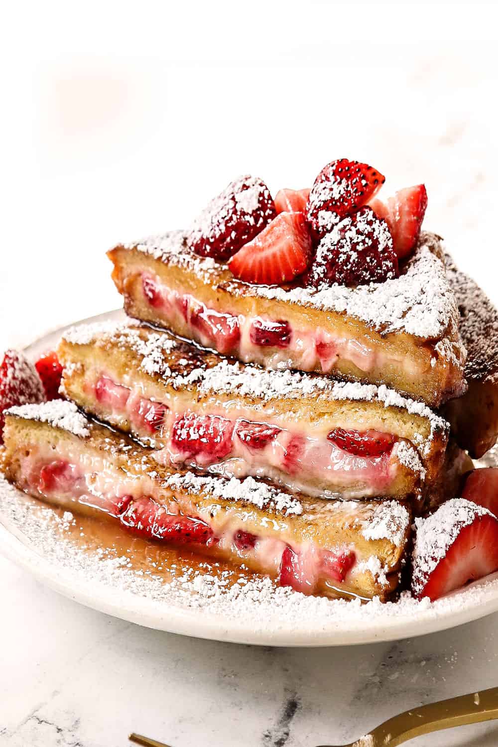 cream cheese stuffed French toast stacked on a plate with strawberries, powdered sugar and syrup